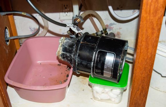 The collar of this under sink garbage disposal completely eroded causing it to crash into the cabinet. Professional plumbing help is needed. Bokeh effect.
